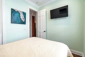 A bedroom with a bed, a wall-mounted TV, and a door leading to another room. - The Lighthouse Group Suite (Key West)