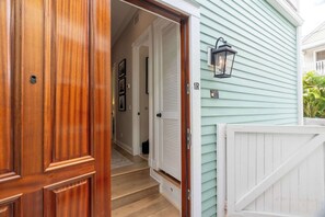 Eine Holztür, die zu einem Flur mit einer Treppe führt, eine weiße Tür mit Fenster sowie eine Leuchte an der Außenwand.