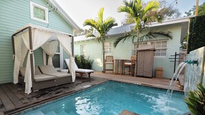 Un patio trasero con piscina, una zona de estar techada y una pequeña cascada.