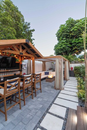 Eine Terrass mit Grillplatz, Sitzgelegenheiten und einem gepflasterten Weg.
