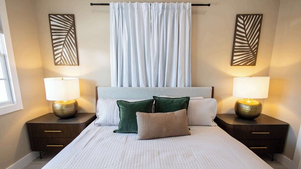 Una habitación de hotel con una cama grande, dos mesitas de noche con lámparas, un cabecero y decoración en la pared.