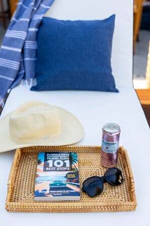 Ein Reiseführer, eine Getränkedose, Sonnenbrille und ein Strohhalm auf einem Tablett auf einem Bett.