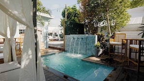 A swimming pool with a waterfall feature, surrounded by wooden deck chairs and a white building. - TortugasHarbor Light Suite (Key West)