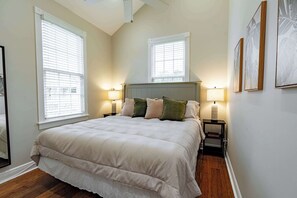 A bedroom with a large bed, two bedside tables with lamps, and three windows with blinds. - TortugasHarbor Light Suite (Key West)