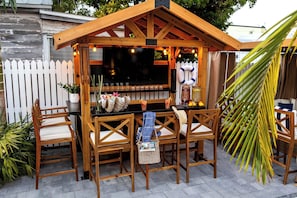A wooden outdoor bar area with a black countertop, two wooden chairs, and a white picket fence in the background. - TortugasHarbor Light Suite (Key West)