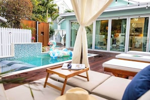 Ein Poolbereich mit Holzterrasse, Liegestühlen und einem kleinen Tisch mit Hut.