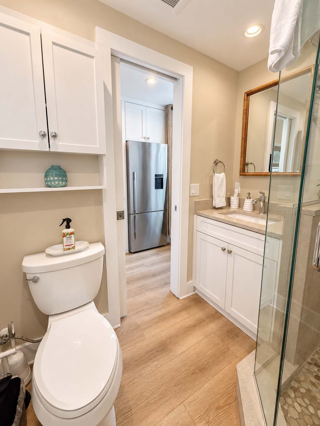 Ein modernes Badezimmer mit Toilette, einer Duschkabine aus Glas und einem Edelstahl-Kühlschrank, der durch einen offenen Durchgang sichtbar ist.
