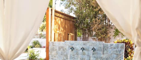Une piscine dotée d’un mur en pierre et de trois jets d’eau, entourée d’une terrasse en bois et de mobilier d’extérieur.