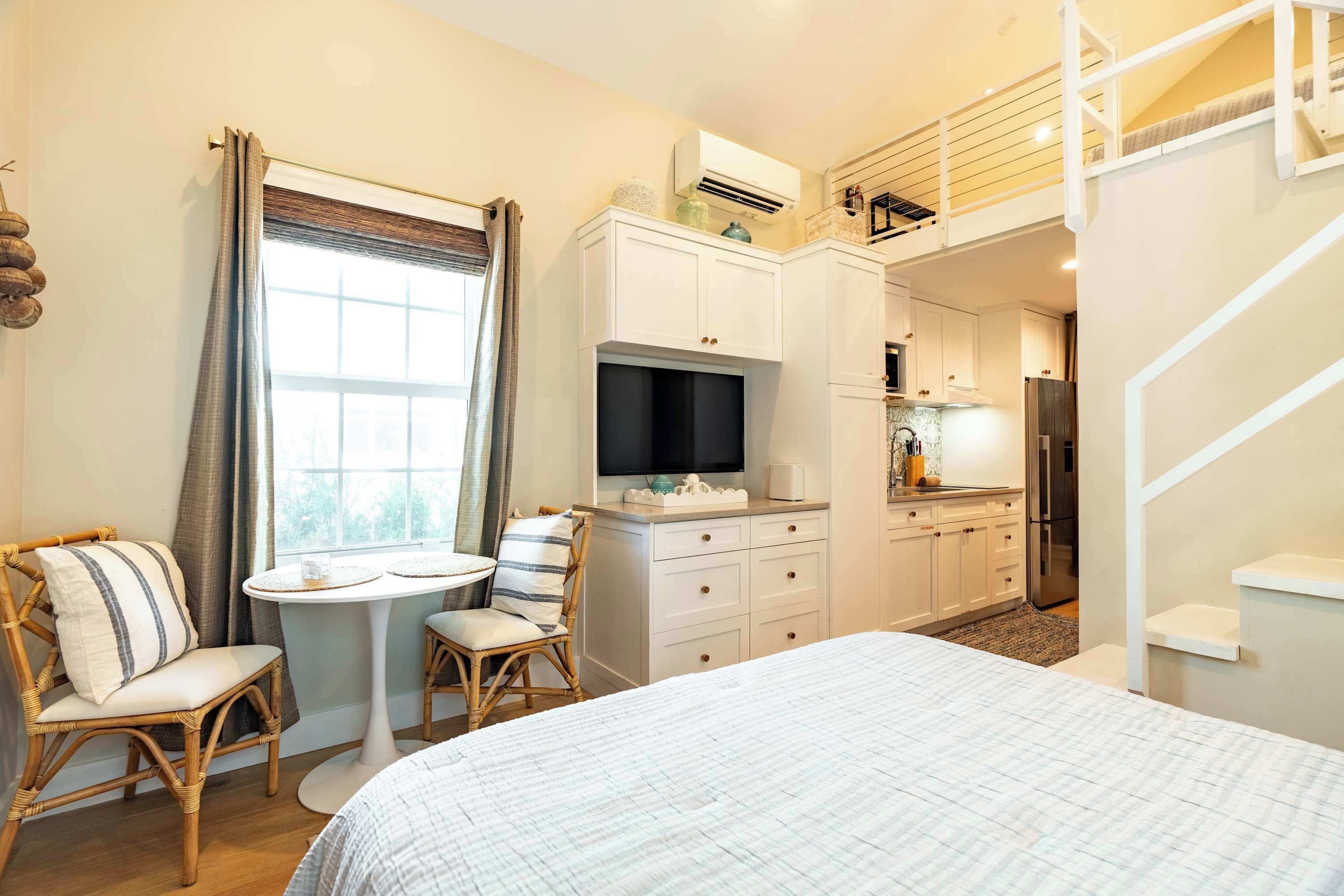 A bedroom with a bed, a small round table, two chairs, a TV, and a kitchenette.