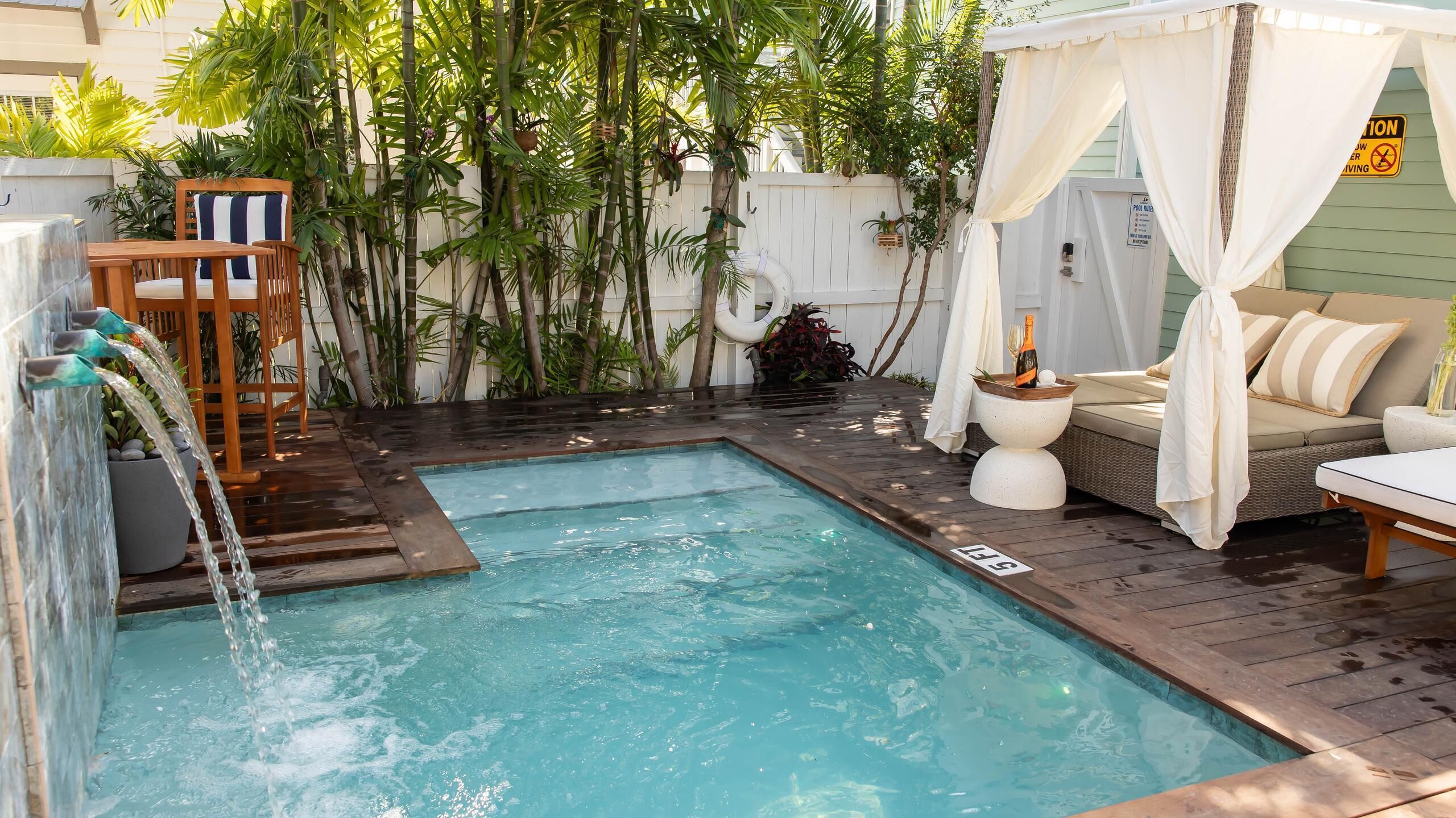 Un área de piscina con terraza de madera, un jacuzzi pequeño y una zona de estar con toldo.