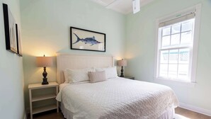Een slaapkamer met een groot bed, twee nachtkastjes met lampen, een schilderij van een vis in een lijst, en een raam met uitzicht.