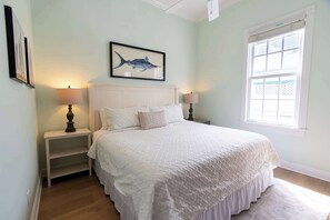 A bedroom with a large bed, two bedside tables with lamps, a framed fish painting, and a window with a view. - American Shoal Light Suite (Key West)