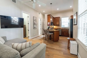 A modern living room with a flat-screen TV, a sofa, and a dining area with a kitchen in the background. - American Shoal Light Suite (Key West)