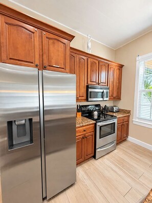 A kitchen with wooden cabinets, stainless steel appliances, and a window with blinds. - Alligator Reef Light Suite (Key West)