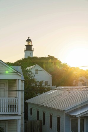 Ein Küstengebäude mit einem Leuchtturm im Hintergrund, umgeben von Bäumen und anderen Wohnhäusern.