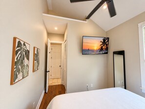 A bedroom with a bed, a TV on the wall, and a door leading to another room. - The Lighthouse Penthouse Suite (Key West)