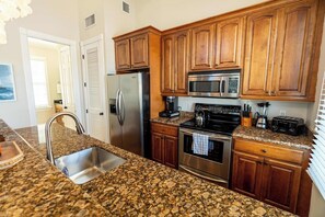 A kitchen with granite countertops, stainless steel appliances, wooden cabinets, and a built-in oven. - The Lighthouse Penthouse Suite (Key West)