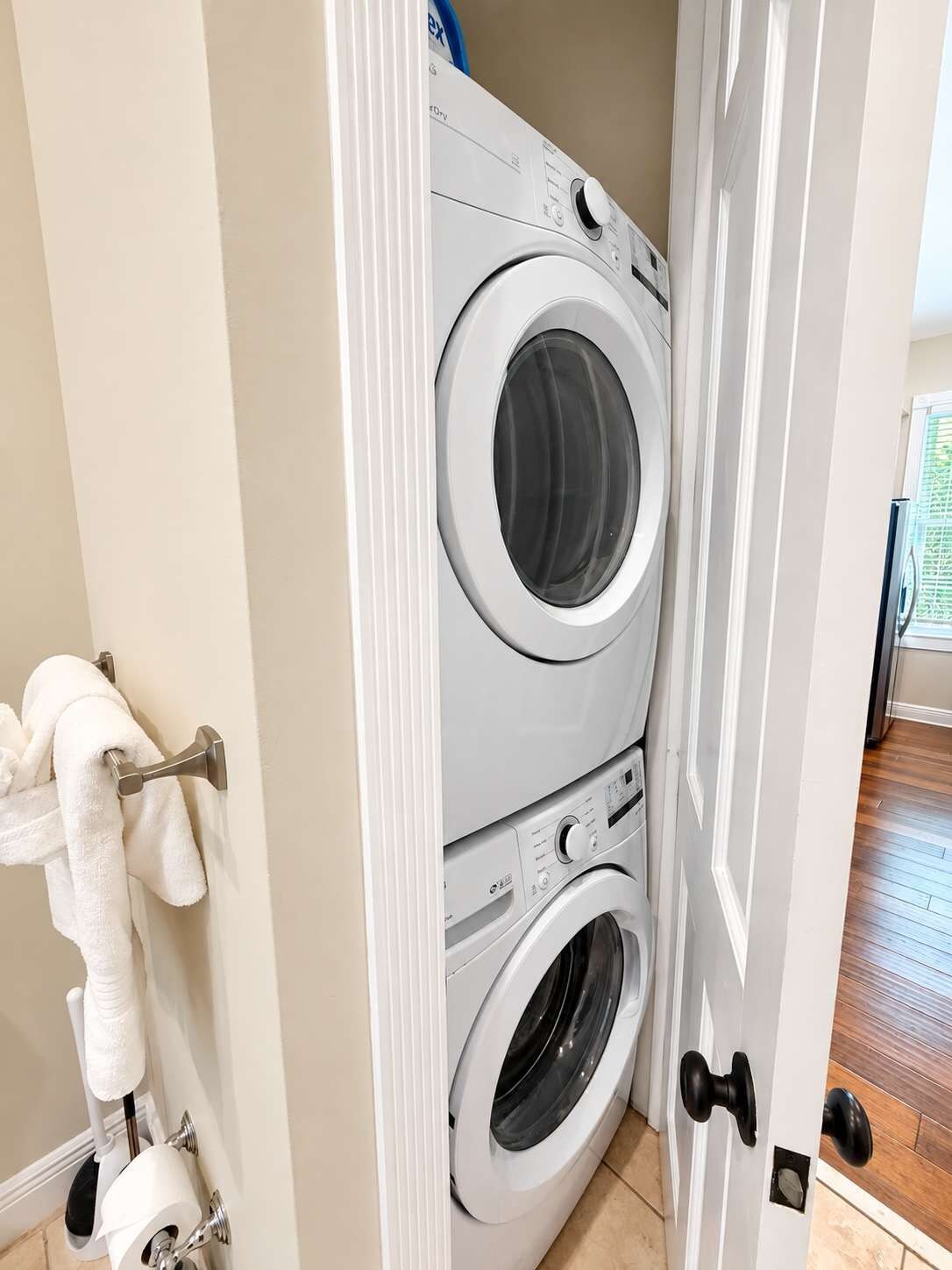 Une buanderie équipée d’un lave-linge et d’un sèche-linge superposés, d’un porte-serviettes avec une serviette et d’un support à papier toilette.