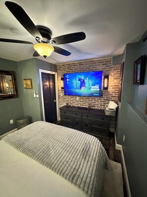 A bedroom with a bed, a dresser, a television mounted on a brick wall, and a ceiling fan. - Stunning Chalet 5-bedroom house in peaceful Lake Harmony with AC (Lake Harmony)