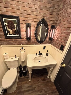 Et badeværelse med murstensvæg, et indrammet billede, et spejl, en vask og et toilet.