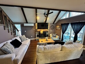 A living room with a fireplace, a ceiling fan, and a large window with curtains. - Stunning Chalet 5-bedroom house in peaceful Lake Harmony with AC (Lake Harmony)