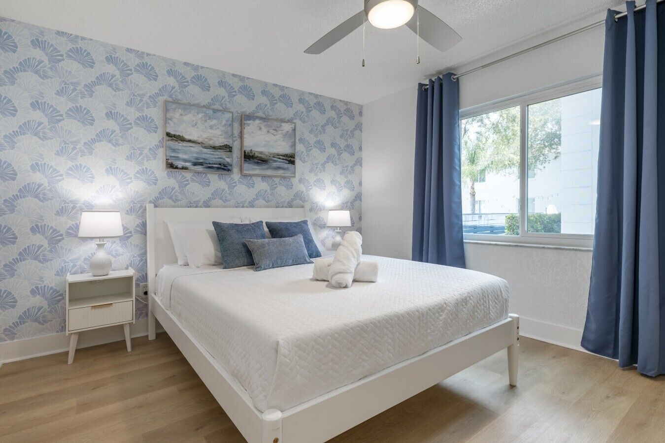 A bedroom with a bed, nightstands, a ceiling fan, and a window with curtains.