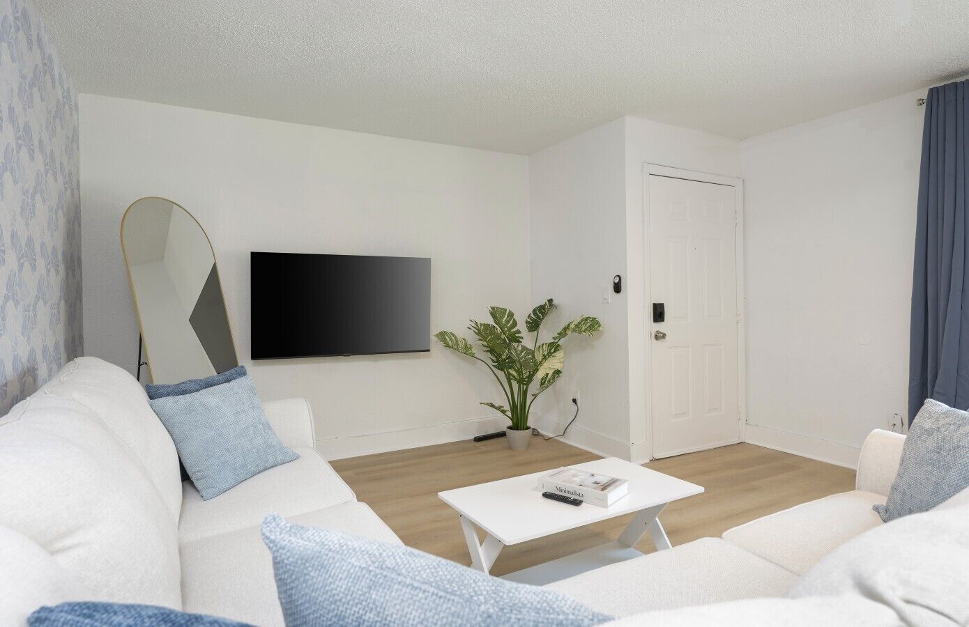 En moderne stue med en hvid sofa, et sofabord, et fladskærms-tv og en potteplante.