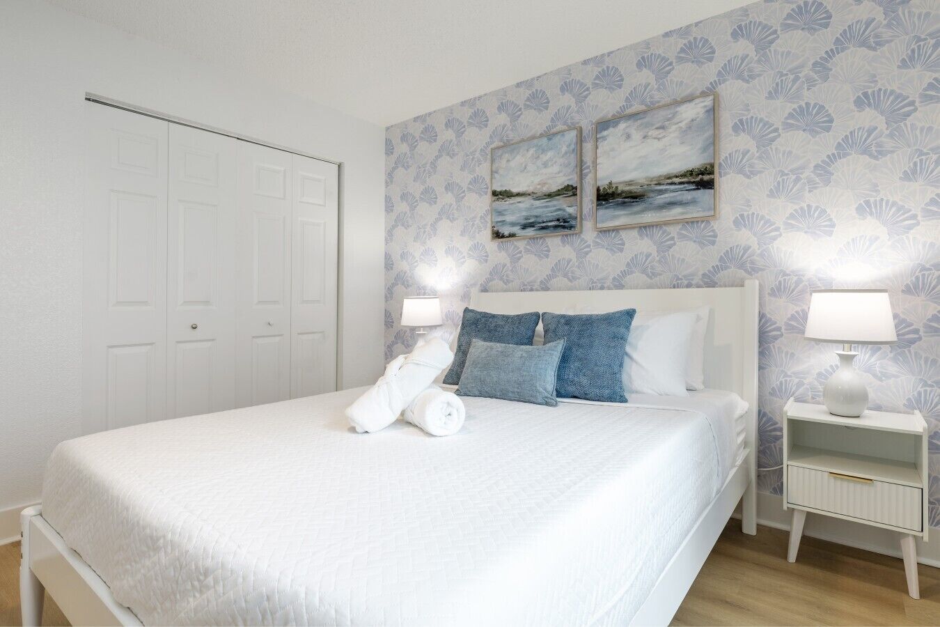 A hotel room with a bed, two nightstands, a white wardrobe, and a wall with a floral pattern.