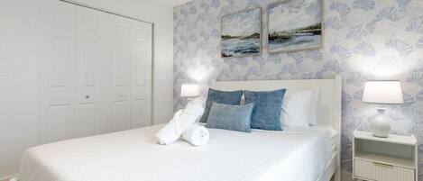 A hotel room with a bed, two nightstands, a white wardrobe, and a wall with a floral pattern.