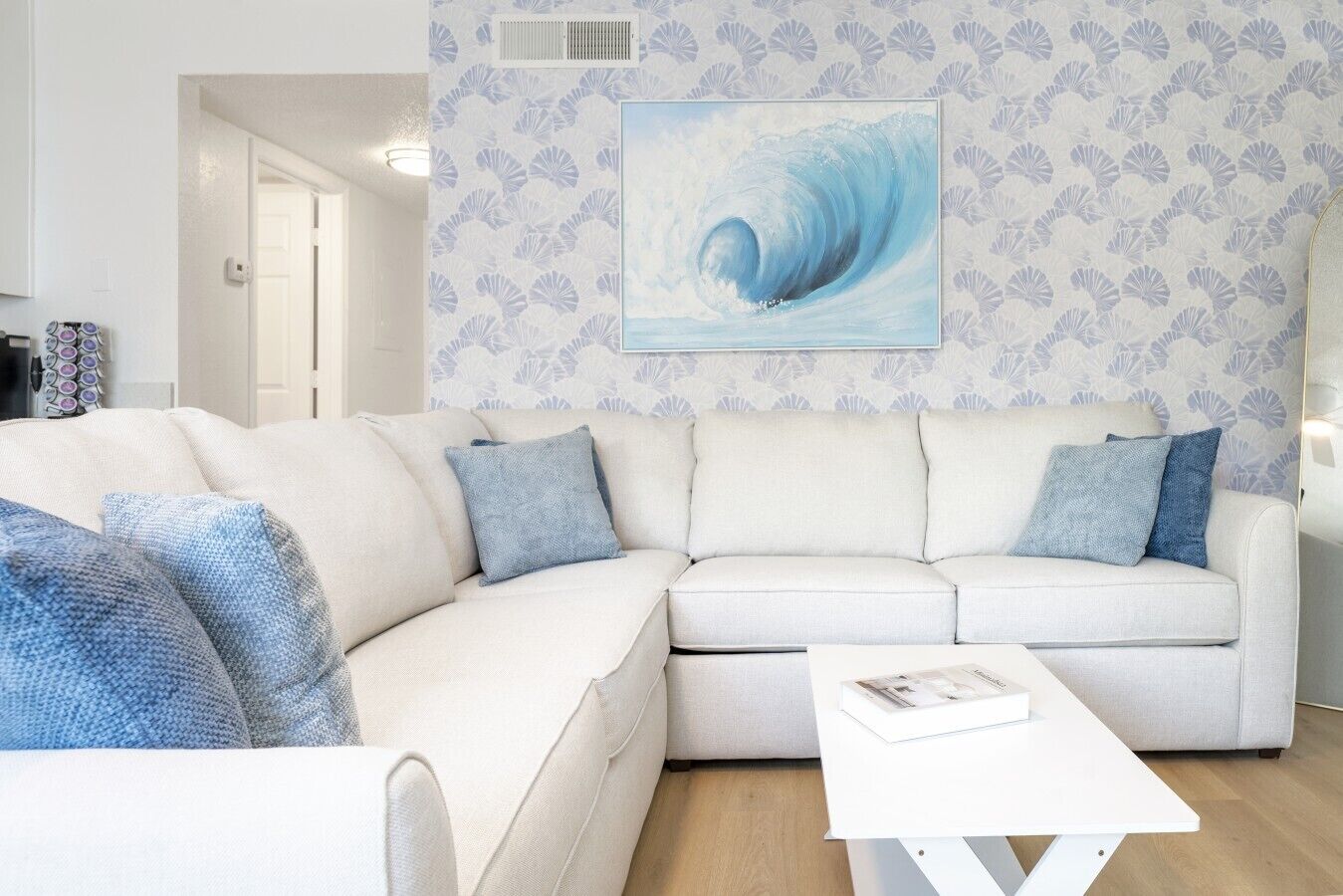 A living room with a white sofa, blue cushions, a white coffee table, and a framed picture of a wave on the wall.