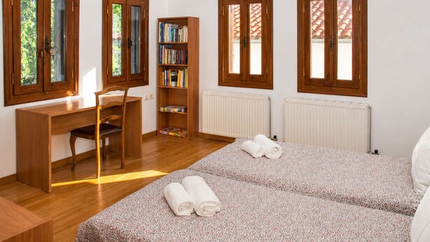 Une chambre avec deux lits, un bureau, une chaise, une bibliothèque et un radiateur.