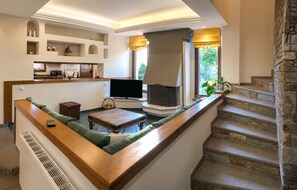 A modern living room with a built-in fireplace, a flat-screen TV, and a stone staircase. - Mountain Breeze Sanctuary With View Near Volos (Volos)