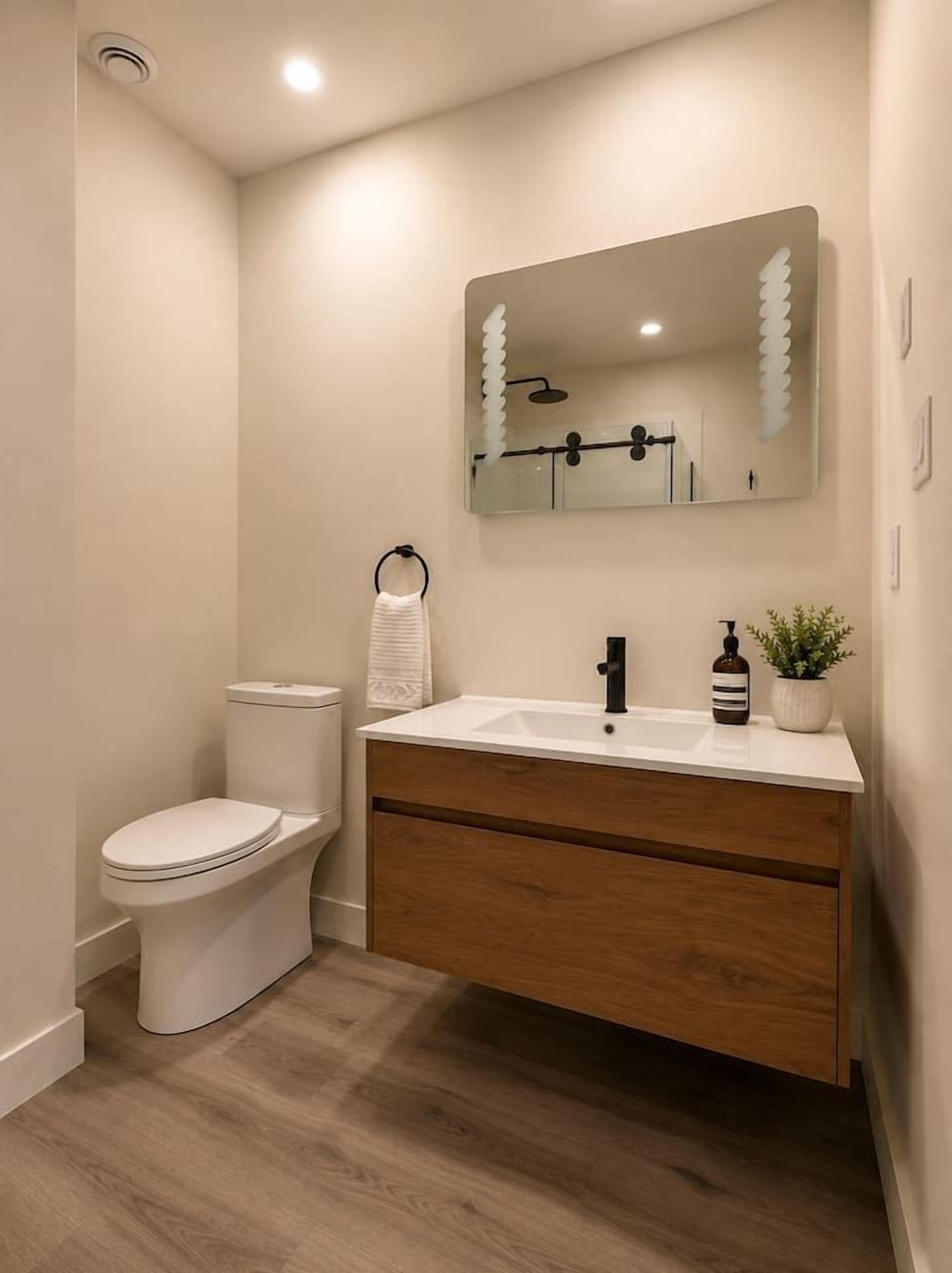 Een badkamer met toilet, wastafel, spiegel en een plant.