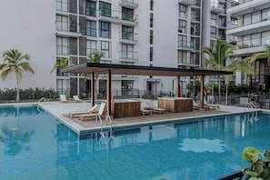 Ein Schwimmbecken mit Liegestühlen und einer Holzterrasse, umgeben von einem modernen Gebäude mit Balkonen.