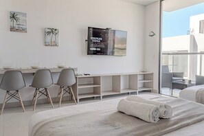 Ein modernes Hotelzimmer mit einem Bett, einem Schreibtisch, drei Stühlen, einem Fernseher und einem Balkon mit Sitzmöbeln.