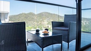 Een balkon met rieten meubels en een tafel, met uitzicht op een bergachtig landschap.