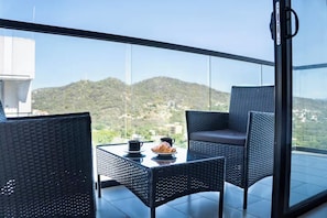 Ein Balkon mit Korbmöbeln und einem Tisch, mit Blick auf eine gebirgige Landschaft.