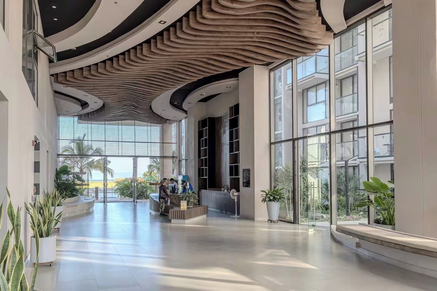 A spacious lobby with a modern ceiling design, large windows, and indoor plants.