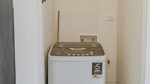 Een compacte, witte wasmachine in een kleine, betegelde ruimte met een enkel stopcontact aan de muur.