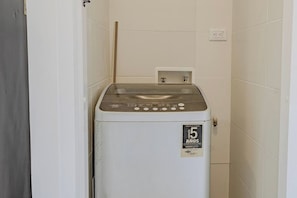 Eine kompakte, weiße Waschmaschine in einem kleinen, mit Fliesen ausgelegten Raum mit einer einzelnen Steckdose an der Wand.