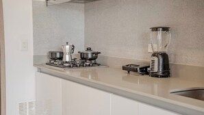 Een keuken met een gasfornuis, twee pannen, een koffiezetapparaat en een blender.