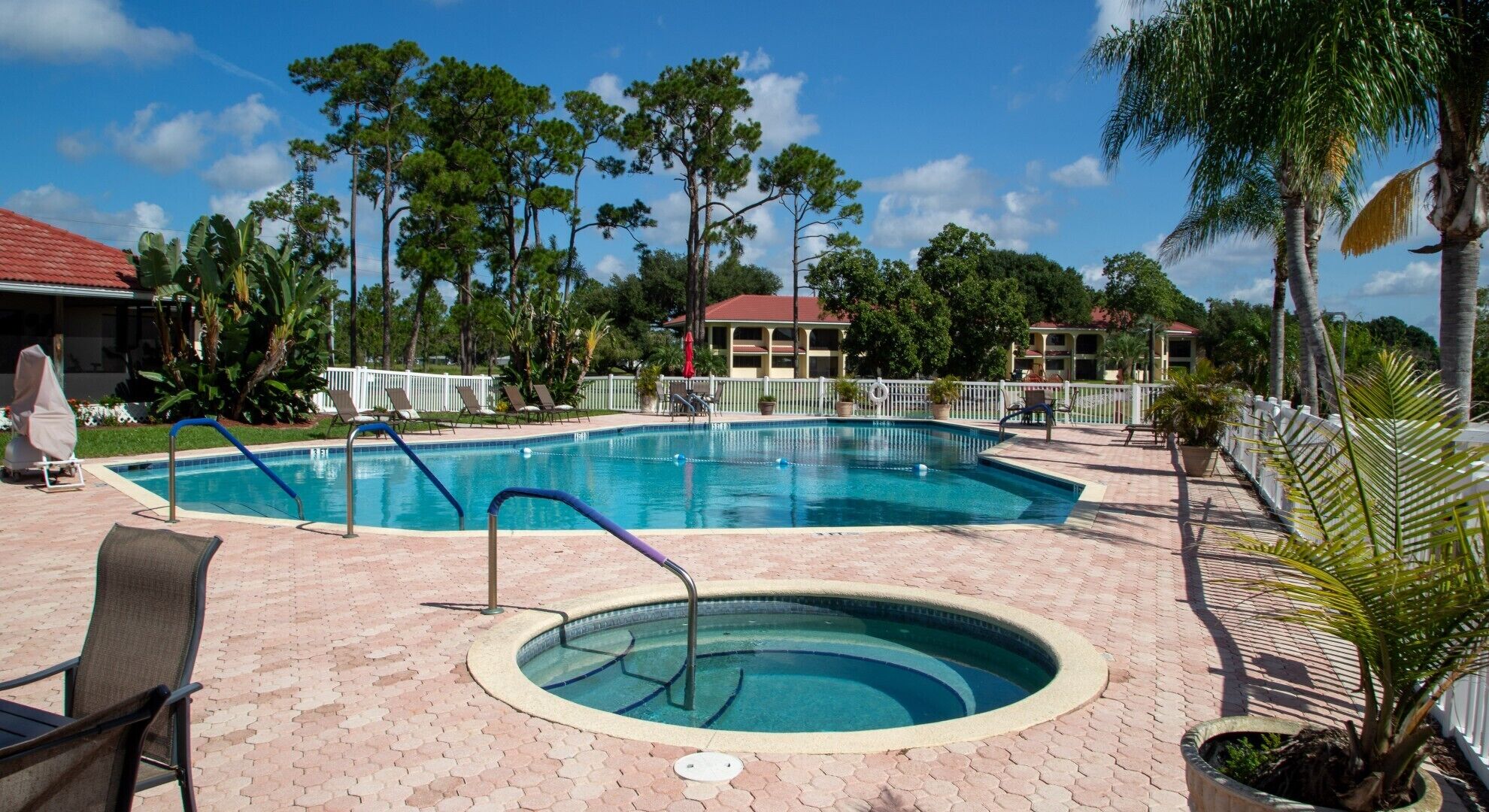 A swimming pool with a surrounding deck, lounge chairs, and a small hot tub.