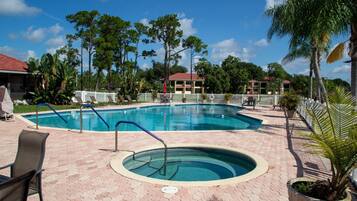 A swimming pool with a surrounding deck, lounge chairs, and a small hot tub.