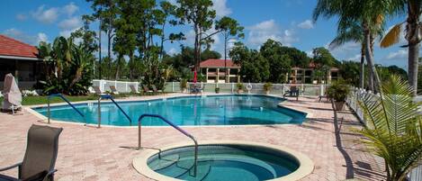 A swimming pool with a surrounding deck, lounge chairs, and a small hot tub.