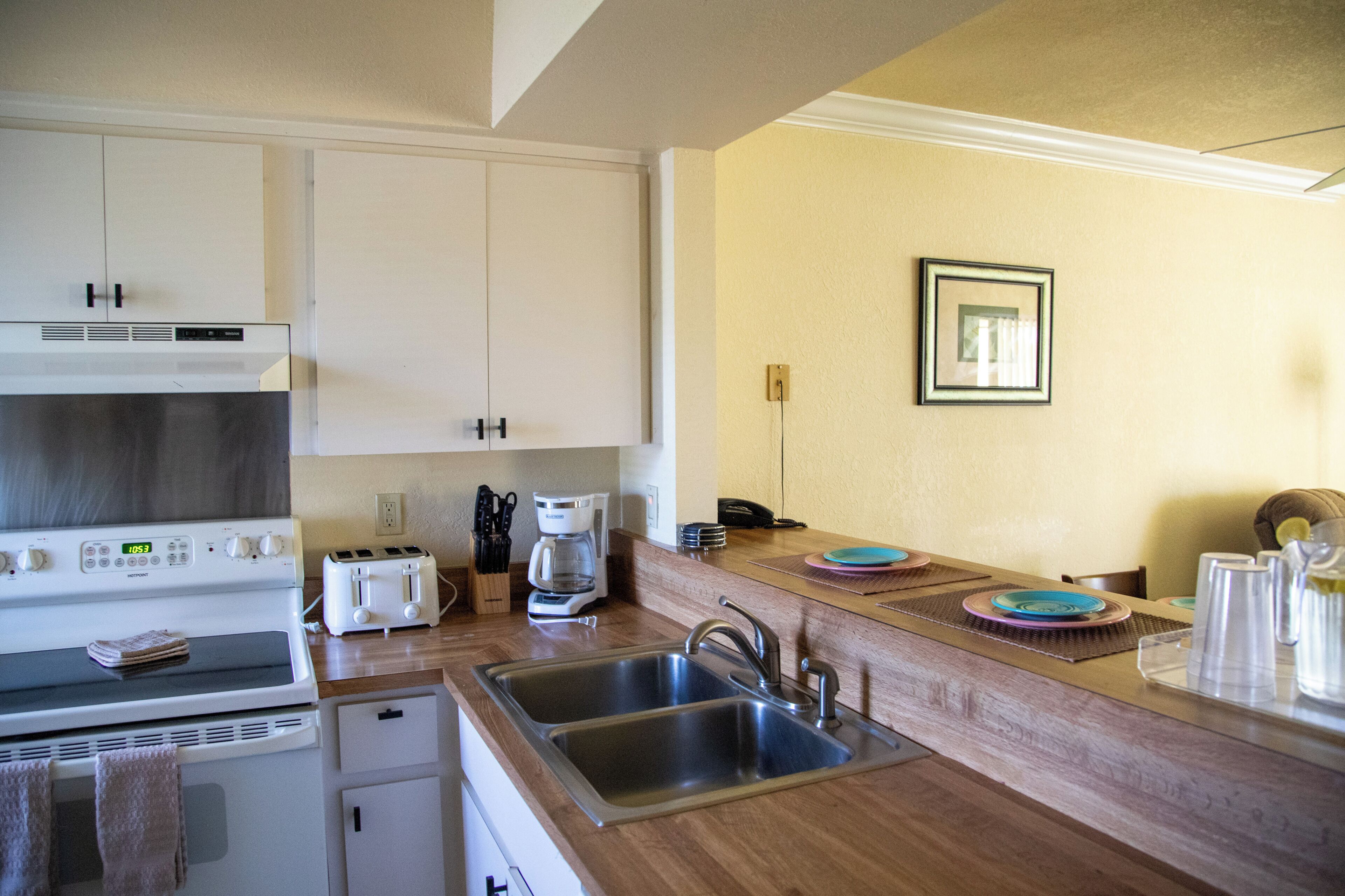 A kitchen with white cabinets, a stove, a toaster, a coffee maker, and a sink.