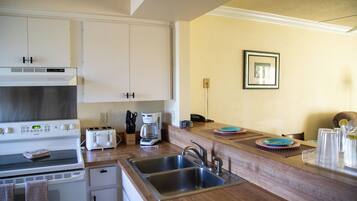 A kitchen with white cabinets, a stove, a toaster, a coffee maker, and a sink.