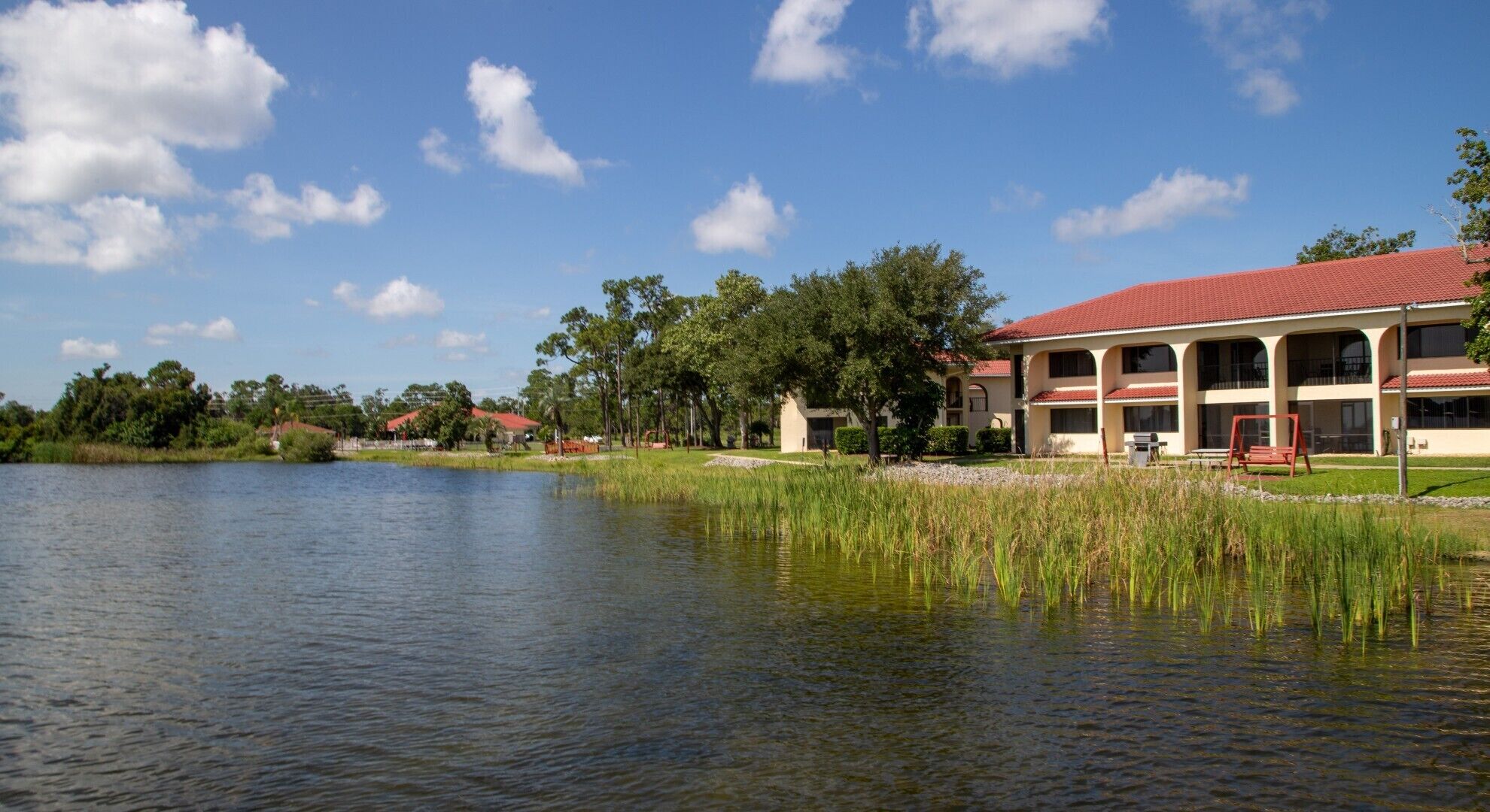 A lakeside hotel with a red roof, multiple windows, and a swing set.