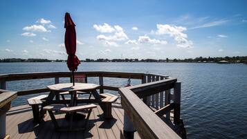 A wooden deck with picnic tables and a red umbrella, overlooking a calm body of water.