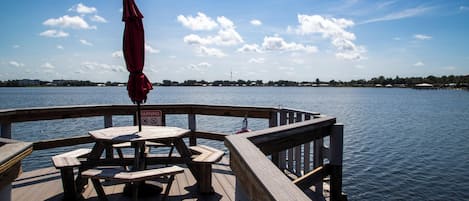 Una terraza de madera con mesas de picnic y un paraguas rojo, con vistas a un cuerpo de agua tranquilo.