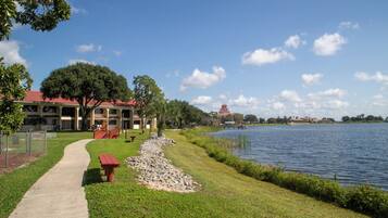 A lakeside walkway with a picnic table, a building with a red roof, and a tower structure across the water.